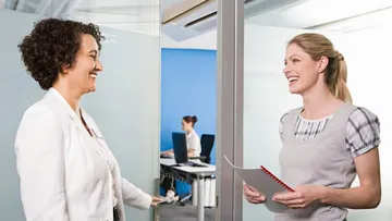 Zwei Frauen reden lachend vor einem Büro miteinander.