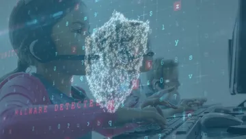 Eine Person tippt am Computer, über dem ein digitales Sicherheitssymbol erscheint.