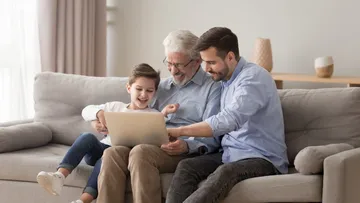 Fünf Personen sitzen auf dem Boden und arbeiten an einem etwas mit Papier und Stiften. Eine trägt ein gelbes Shirt und zeichnet. Die anderen schauen zu und tragen bunte Kleidung. Der Raum ist hell mit roten Kissen.