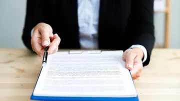 Eine Person gibt ein Dokument und einen Stift zum Unterschreiben.