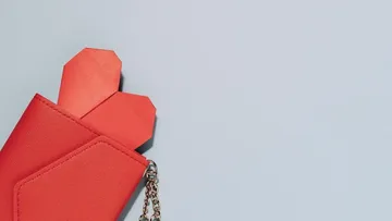 Aus einer roten Geldbörse schauen zwei Papierherzen heraus.