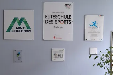 Blick auf die Wand im Forum der Schule, an der die wichtigesten Siegel und Partner der Schule gewürdigt werden.