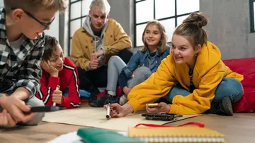 Drei Personen sammeln Müll in einem Park mit Bäumen. Ein Kind mit pinker Mütze füllt einen roten Sack. Eine Erwachsene und ein weiteres Kind helfen mit.