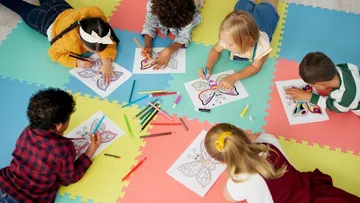 Kinder malen Schmetterlingsbilder. Dazu benutzen Buntstifte und Filzstifte. Sie liegen auf blauen, rosa und gelben Schaumstoffmatten und tragen bunte Kleidung.