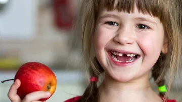 Ein fröhliches Mädchen mit fehlenden Zähnen hält einen Apfel.