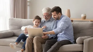 Fünf Personen sitzen auf dem Boden und arbeiten an einem etwas mit Papier und Stiften. Eine trägt ein gelbes Shirt und zeichnet. Die anderen schauen zu und tragen bunte Kleidung. Der Raum ist hell mit roten Kissen.
